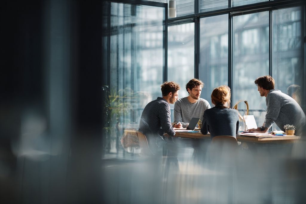 Image d'un bureau où des professionnels discutent autour d'une table, illustrant l'esprit collaboratif et innovant.